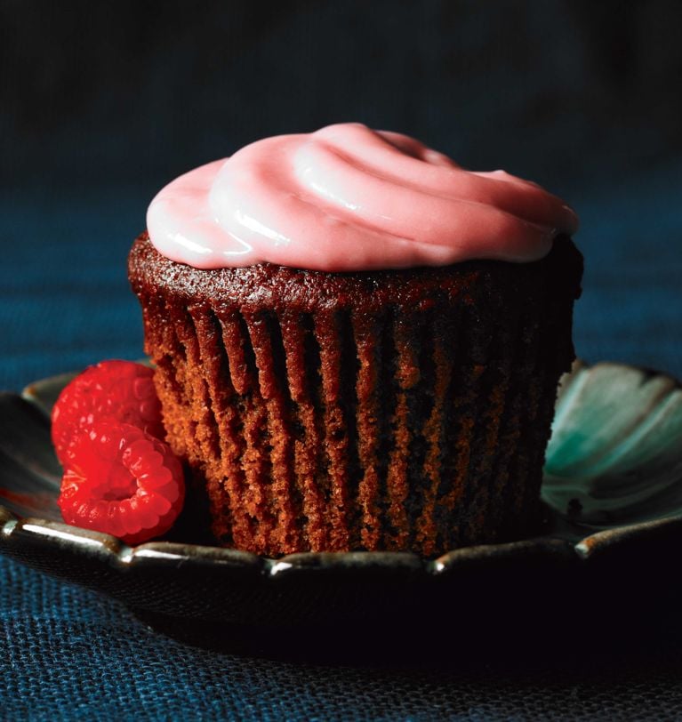Velvety beet cupcakes with raspberry icing on a green saucer next to fresh raspberries