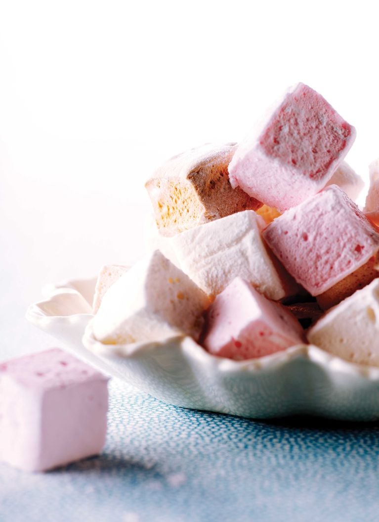 A scalloped white bowl holding homemade marshmallows that are pink and white