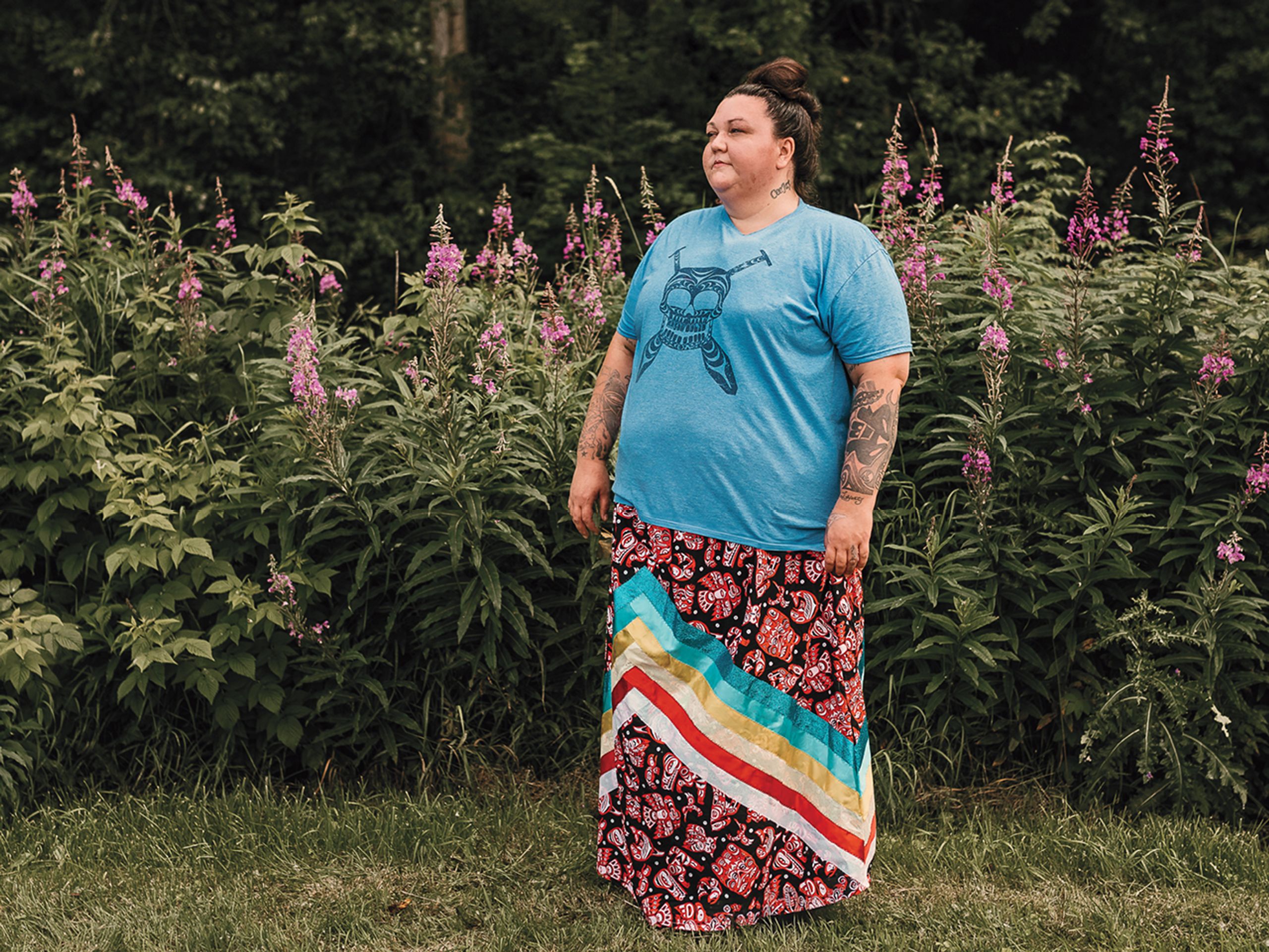 Amanda Lepine stands in a field, wearing a light-blue T-shirt and a ribbon skirt. Lepine participated in the Mother-Child Program while incarcerated in B.C.