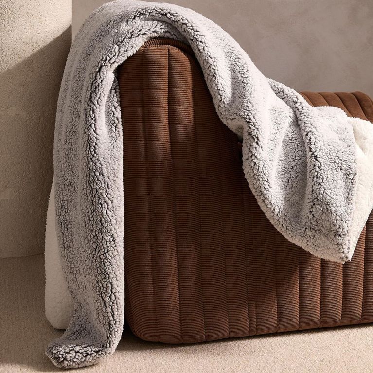 A grey fleece plush reversible throw blanket draped over a brown couch, for a post about the best gifts for book lovers.