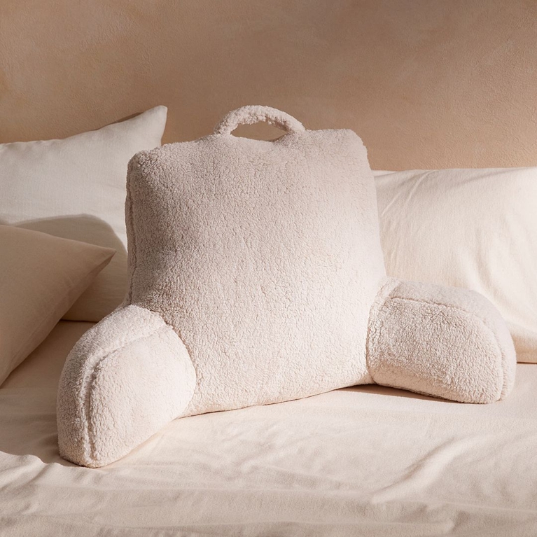 A white fleece reading pillow on a bed with white linens, for a post about the best gifts for book lovers.