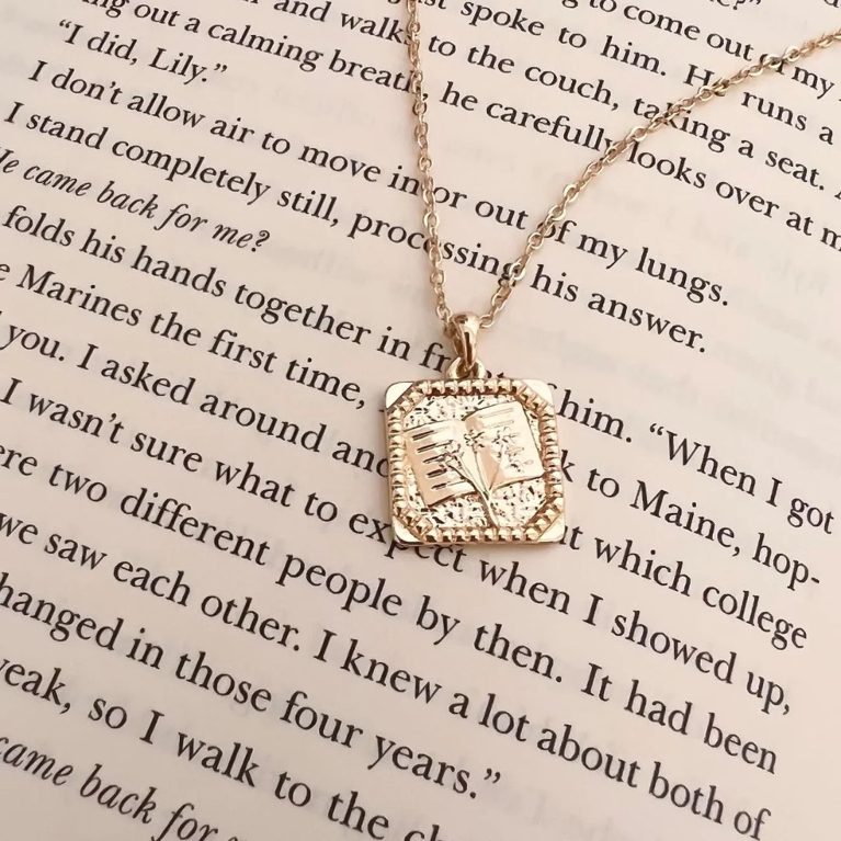 A gold floral book necklace sitting atop a page in an open book, for a post about the best gifts for book lovers.