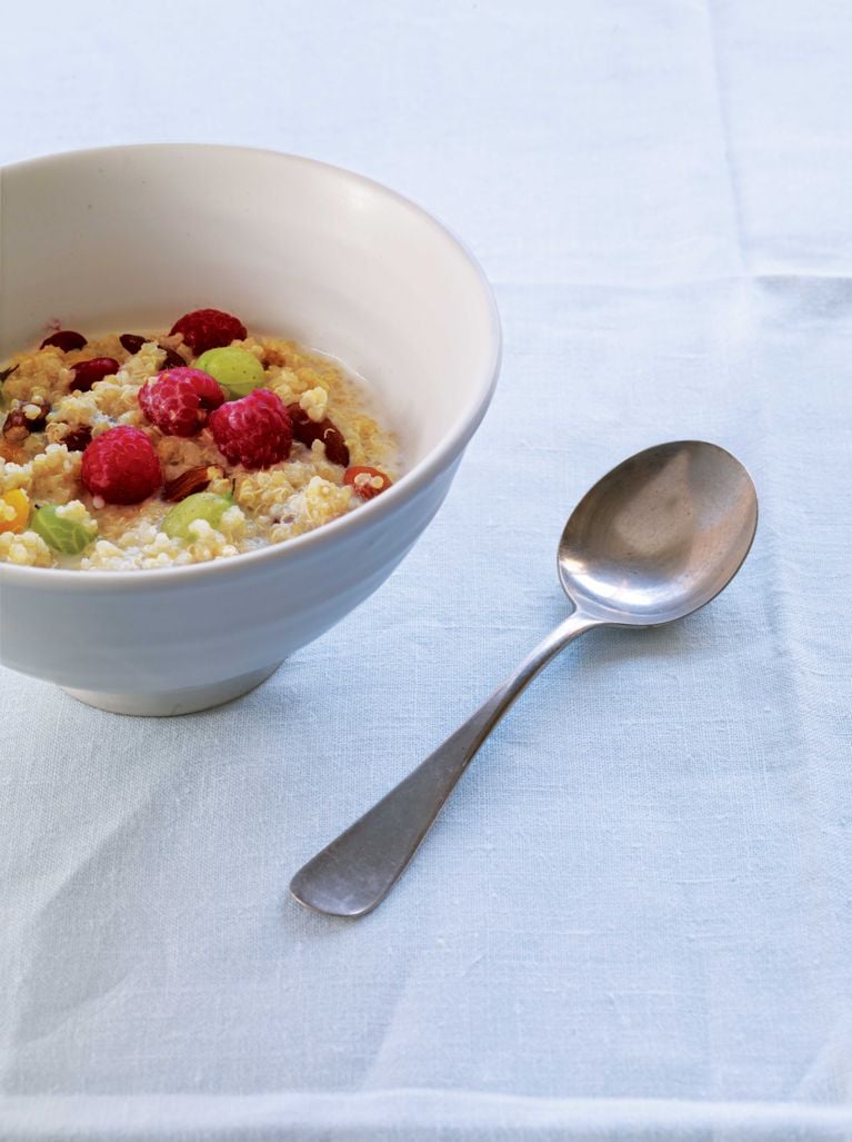 A bowl of quinoa cooked with almond milk cardamon, raisins, almonds and apricots topped with fresh raspberries for a post on an easy, healthy quinoa porridge breakfast recipe