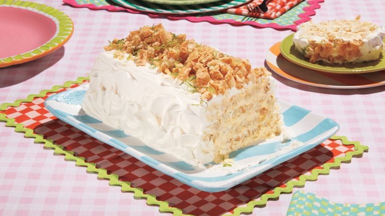 A rectangular cake made with layers of mango and lime cream, strips of puff pastry, frosted with whipped cream and tipped with crunchy toasted coconut flakes.