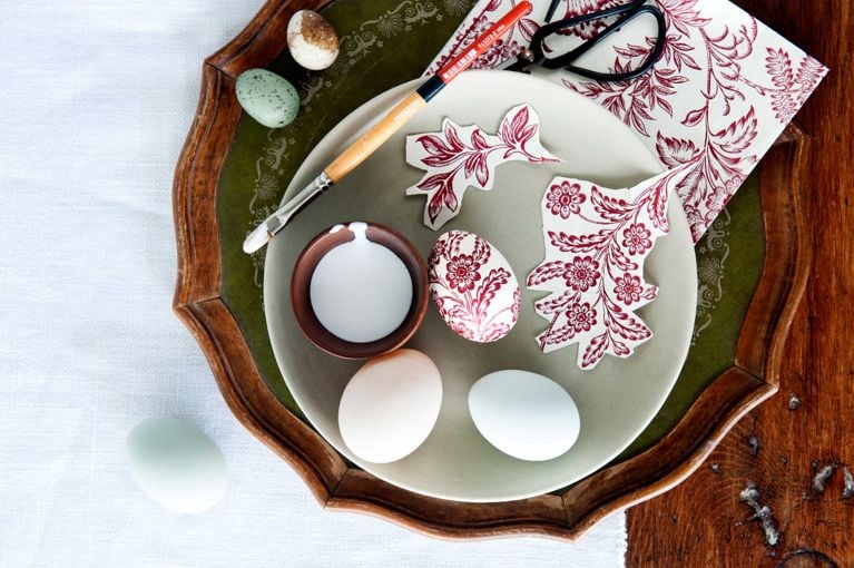 A bowl of eggs and a pot of glue getting decorated with cut out paper napkins for an easy, pretty way to decorate Easter eggs for a spring centre piece