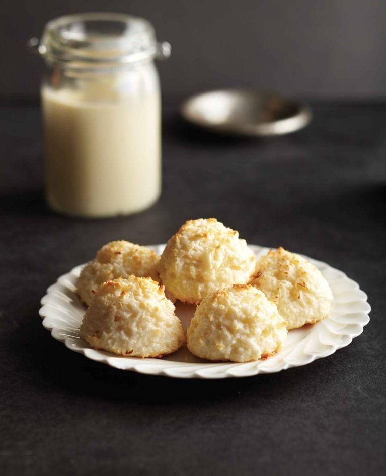a jar of homemade sweetened condensed milk next to a plate of macaroons