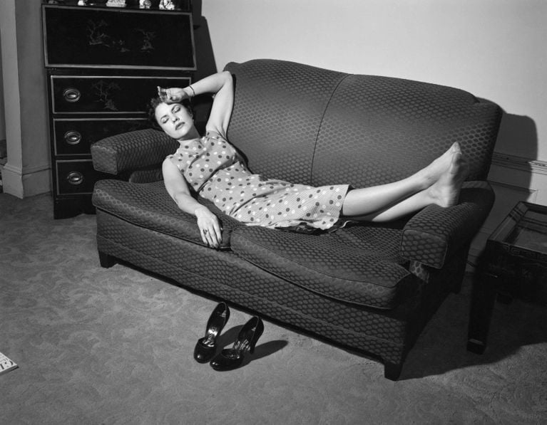 A black and white 1950s image of a woman in a shift dress lying on a couch, her hand to her forehead, a pair of pumps on the carpet next to her, to illustrate a piece about Ontario's new iron deficiency guidelines and what it means for health and in Canada