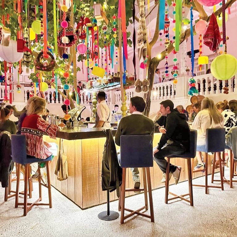 People sitting around a bar in a restaurant that has brightly coloured streamers hanging from the ceiling, in a post about lima peru.