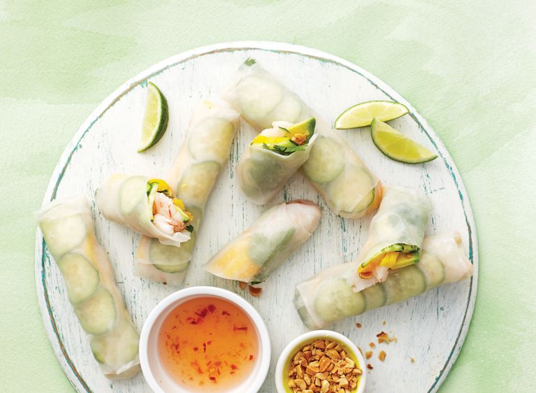 No-cook Shrimp, avocado and mango salad rolls on a plate next to dipping sauce and peanuts; the salad rolls are made with precooked frozen shrimp; rice paper; cucumber; mango; cilantro and Thai dipping sauce for a post on an easy no-cook shrimp avocado mango salad roll recipe