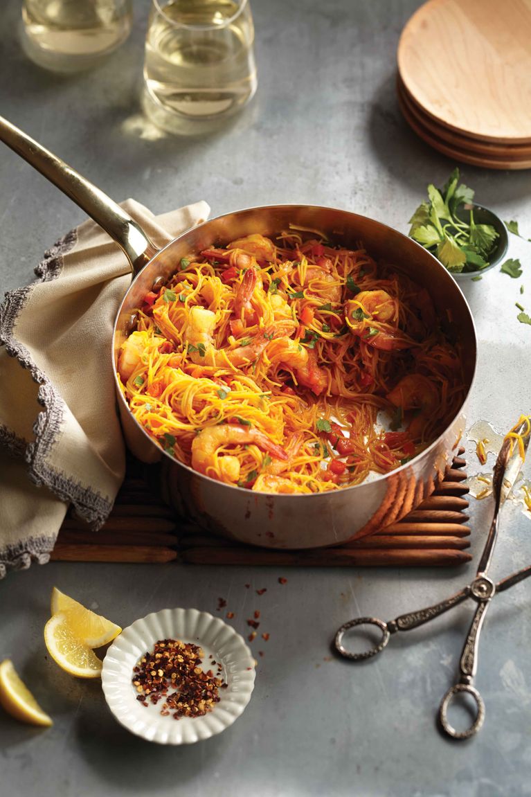 One-pot Spanish shrimp fideuá in a pot on a cooling board, it's made with garlic, onions, tomato paste; paprika; saffron; vegetable broth; 300-g pkg frozen shrimp; thin rice vermicelli; parsley and lemon