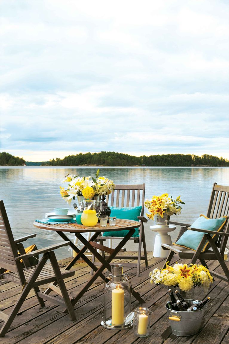 A setting for a dockside party with spiked lemonade in a pitcher on a table next to candles and buckets of flowers