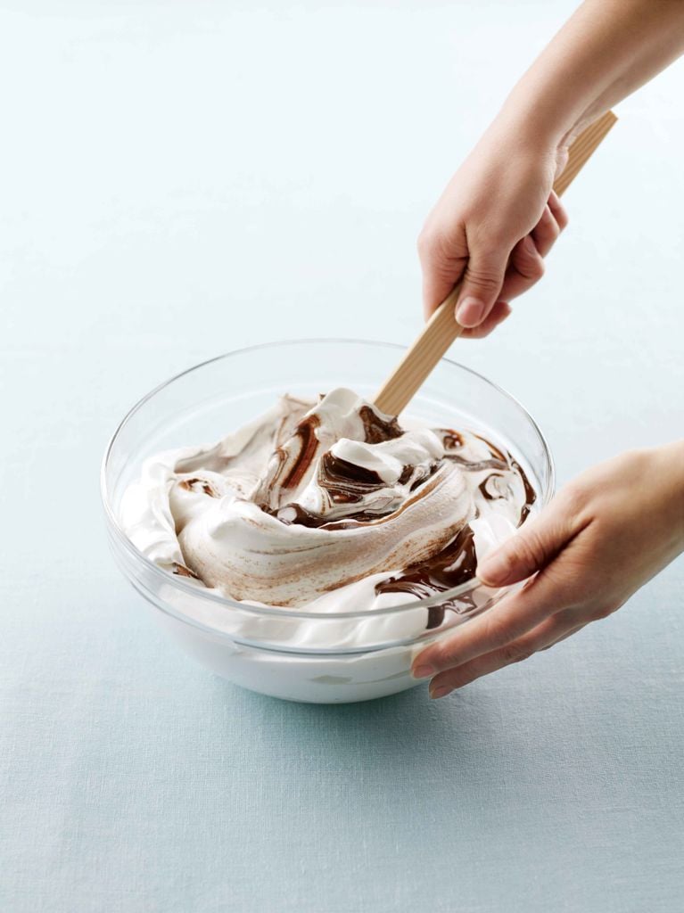 the batter for vanilla-chocolate meringues being stirred in a glass bowl with swirls of chocolate