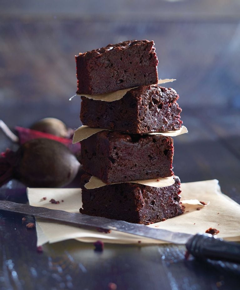 four chocolate-beet brownies stacked on parchment paper