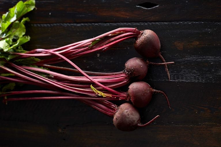 A bunch of beets with their greens lying on a table for a post on how to cook beets and the best beet recipes