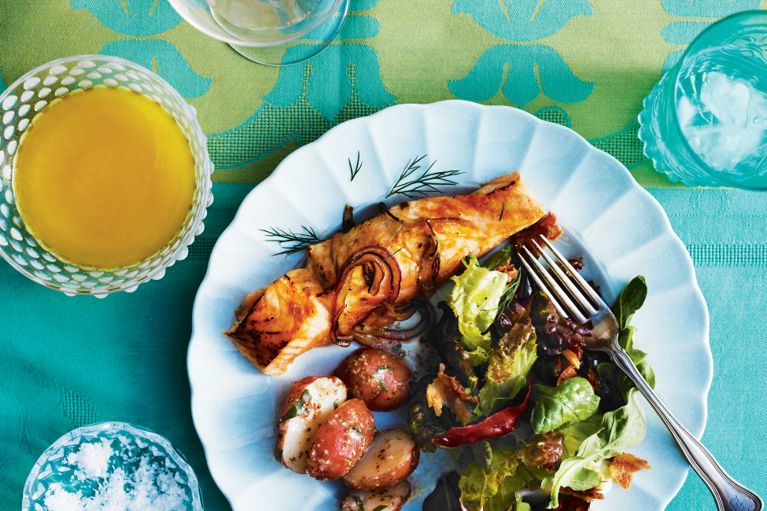 centre-cut, skin-on salmon fillets on a cedar plank cut into slices and grilled and then topped with onions and sprigs of fresh dill for a post on an easy, delicious cedar-plank salmon recipe for the grill served with green salad and red potato salad
