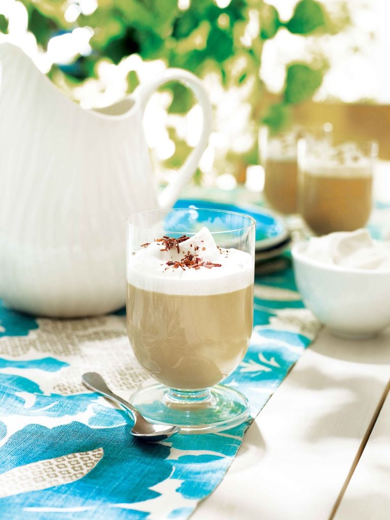 A dulce de leche pudding in a glass next to a spoon; the pudding is made with dulce de leech; whipping cream; sugar; cornstarch; milk and vanilla and garnished with whipped cream and shaved chocolate for a post on an easy dulce de leech pudding recipe