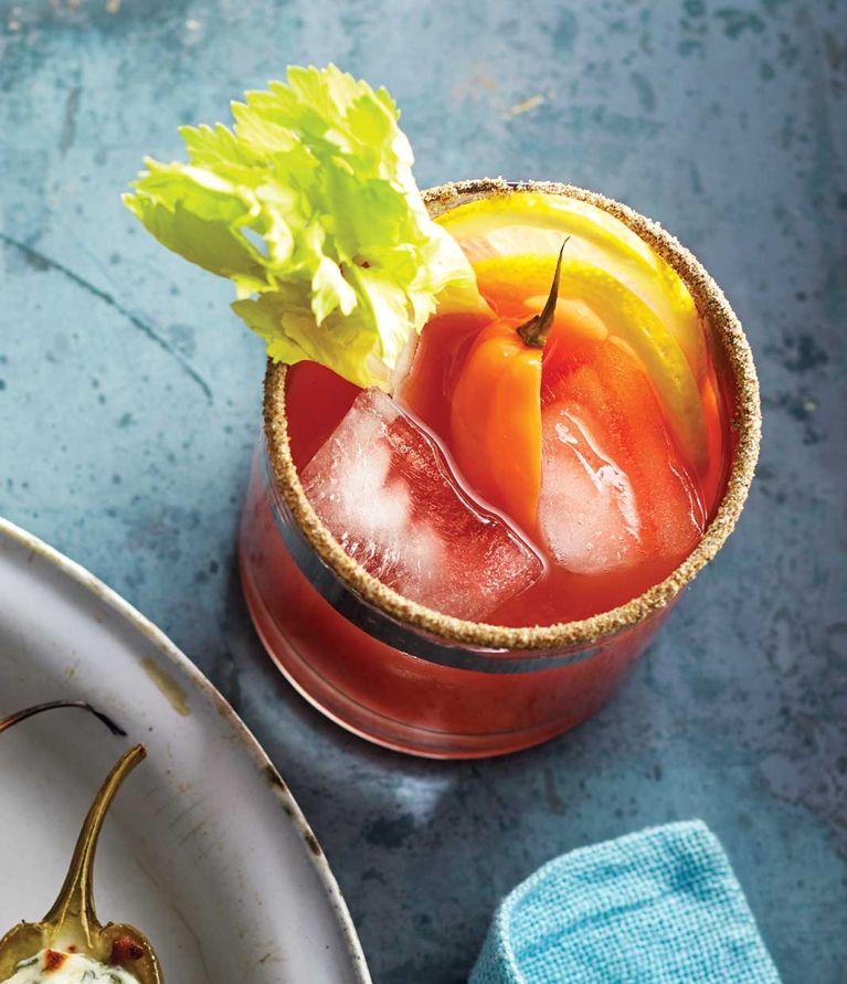 An extra-spicy caesar cocktail recipe made with homemade hot pickled pepper brine, Clamato juice; vodka; lemon; celery stalk; celery stalk; ice cubes and garnished with hot peppers for a post on an easy extra spicy caesar cocktail recipe