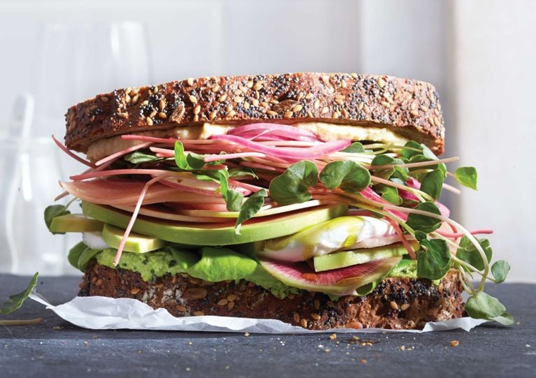 A sandwich made with grainy brown bread, avocado; sprouts and more healthy toppings; the bread is made with molasses; yeast; whole wheat flour; pipits; flax; sunflower seeds; poppy seeds; sesame seeds; salt and egg for a post on an easy healthy homemade grainy brown bread recipe