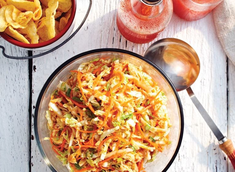 Fresh Kimchi Coleslaw in a bowl next to a serving ladle and chips; the slaw is made with rice vinegar; sugar; miso; ginger; sriracha; garlic; Napa cabbage; grated carrots and green onions for a post on an easy fresh kimchi coleslaw recipe