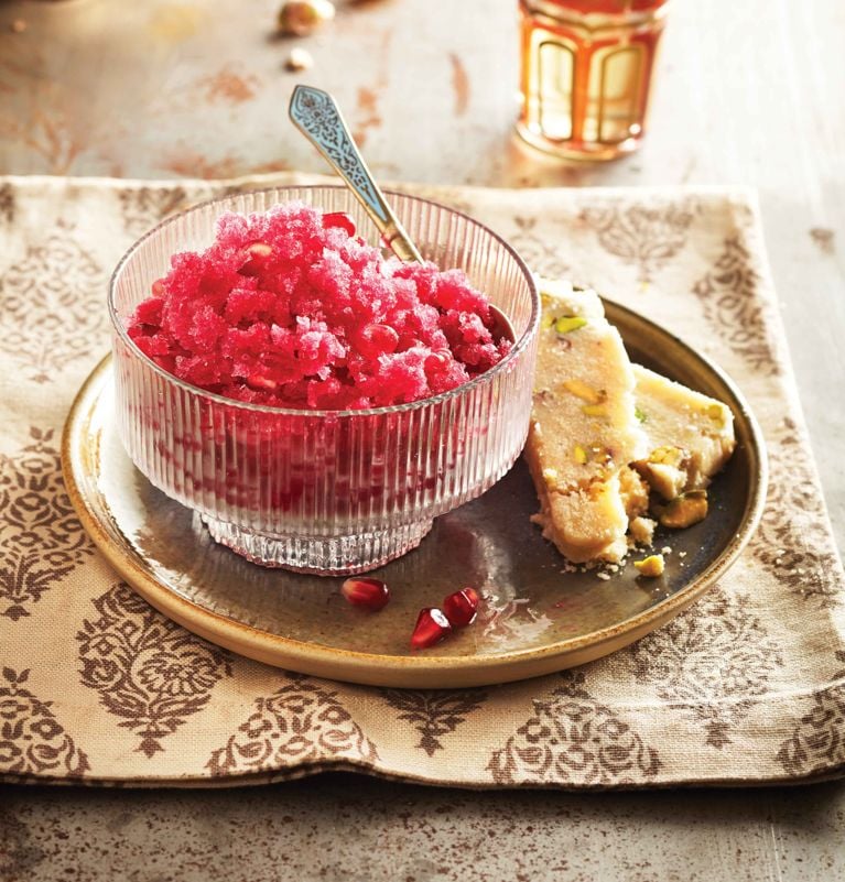 a pomegranate granita in a bowl with a spoon; the granita is made of pomegranate juice; lemon juice; orange flower water and garnished with pomegranate seeds for a post on a cooling pomegranate granita recipe