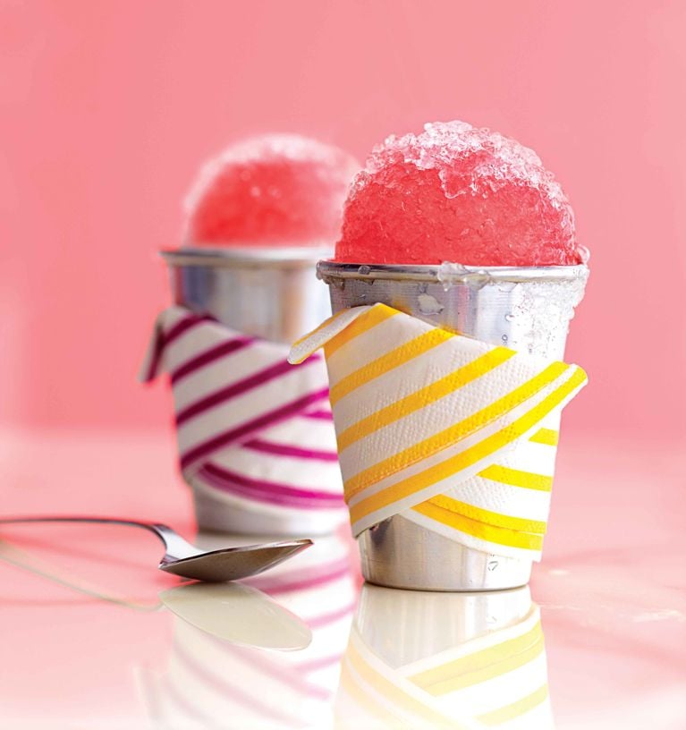 Rhubarb snow cones made with rhubarb syrup in a metal cup with colourful napkin wrappings for a post on an easy summer rhubarb snow cone recipe