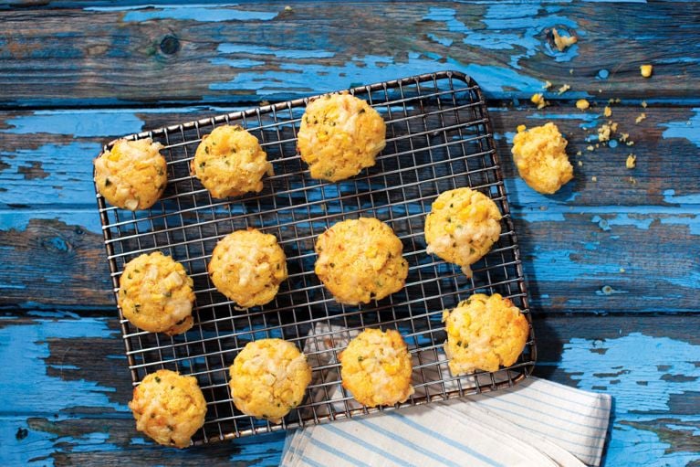 Smoky hush puppies on a cooling rack—yellow corn-filled biscuits made with cornmeal; all-purpose flour; finely chopped jalapeños; grated smoked cheddar; fresh corn kernels; egg; melted butter and milk for a post on an easy smoky hush puppies recipe for biscuits with fresh corn