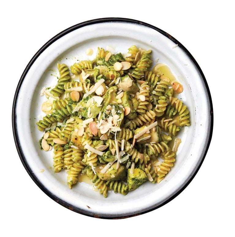 Spinach-pesto and artichoke pasta salad on a plate, made with fusilli pasta; garlic; spinach; sliced almonds; grated parmesan; lemon juice;