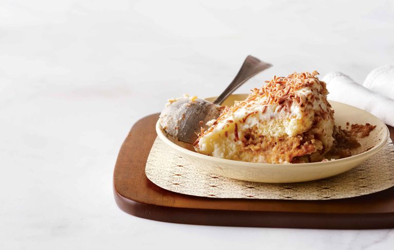 white chocolate espresso tiramisu on a plate next to a spoon; the tiramisu is made with espresso; Kahlúa coffee liqueur; white chocolate; mascarpone; sugar; 35% cream; vanilla; cocoa; giant ladyfingers and shaved chocolate for a post on a. delicious white chocolate espresso tiramisu recipe
