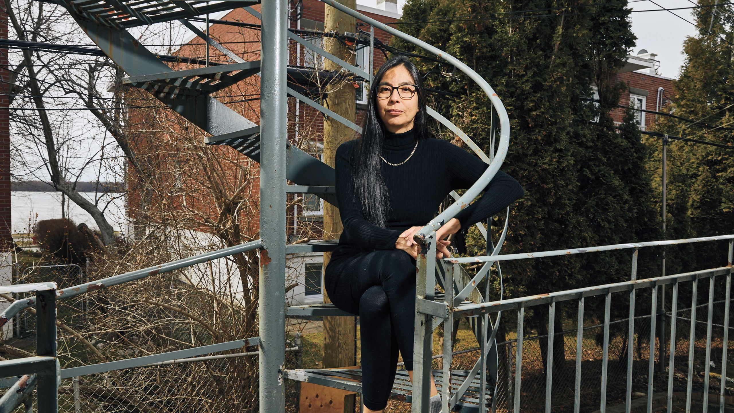 Sheri Pranteau, wearing a black turtleneck and leggings, sits on a spiral staircase at her home in Montreal.