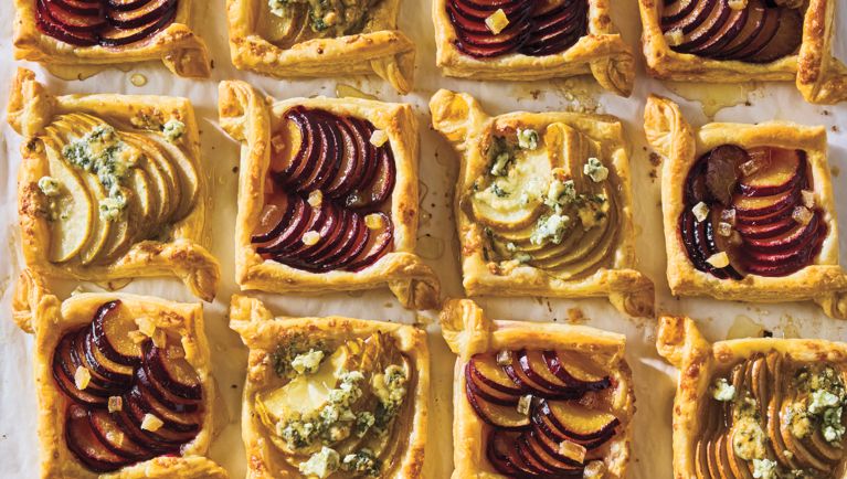 A prepared sheet pan covered in freshly baked puff pastry tarts filled with pear and blue cheese and plum and candied ginger.