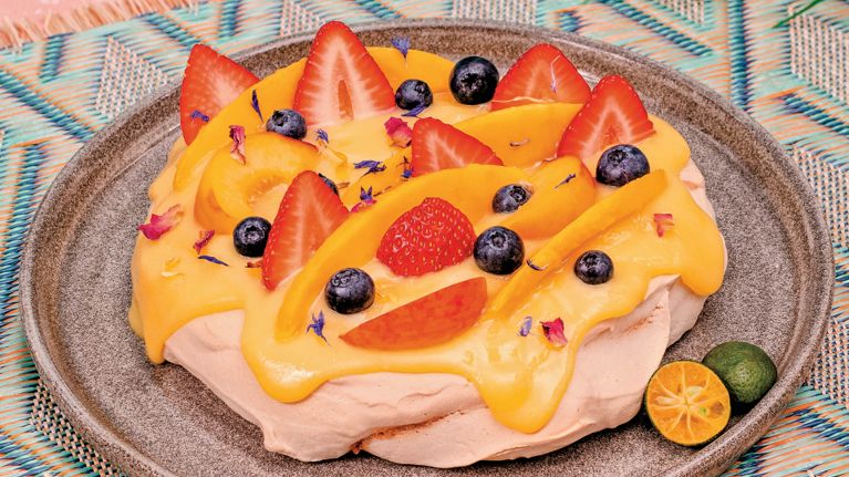 A lightly pink pavlova covered in yellow calamansi curd cream and sliced berries.