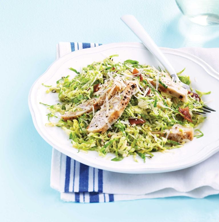 a plate with shredded Brussels sprouts; bacon; chicken breasts; covered with a Caesar salad dressing for a post on an easy weeknight Brussels sprouts chicken Caesar salad recipe