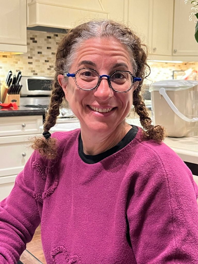 A photo of a woman with braids and a pink sweater, in a kitchen.