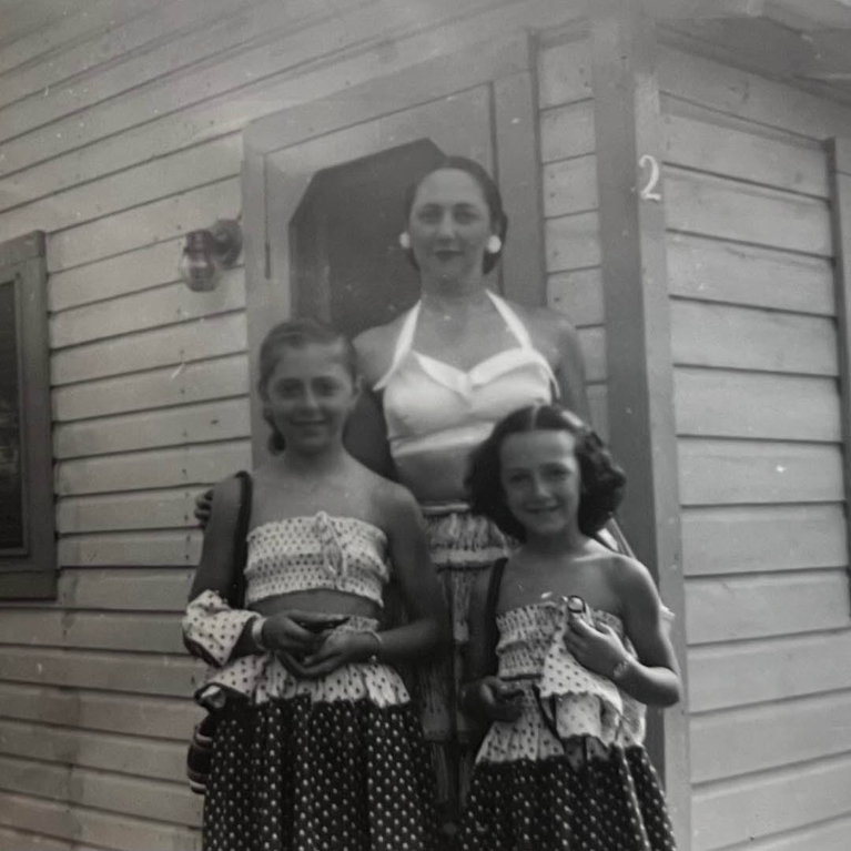 A black and white photo of a woman in a white halter top with two young girls in matching polka dot outfits.