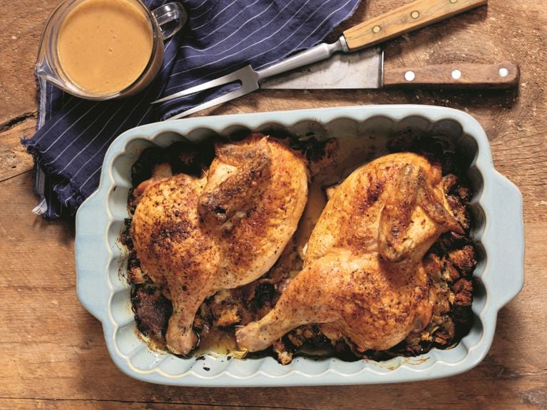 A roasting dish filled with stuffing and two halves of a chicken.