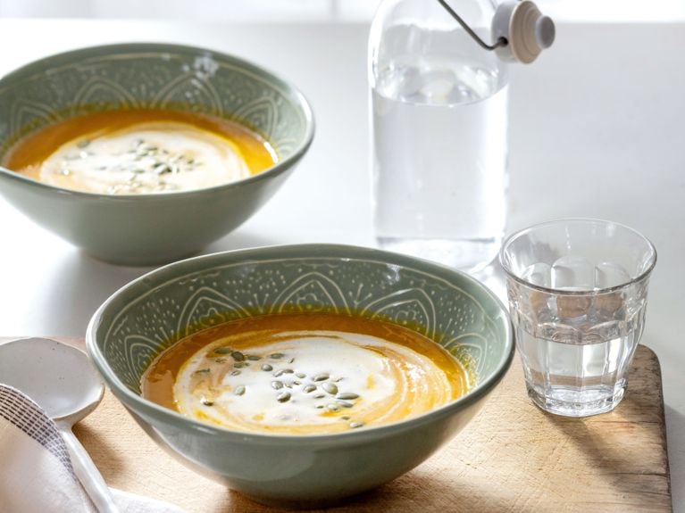 Two bowls filled with spiced carrot soup and garnished with a drizzle of cream.