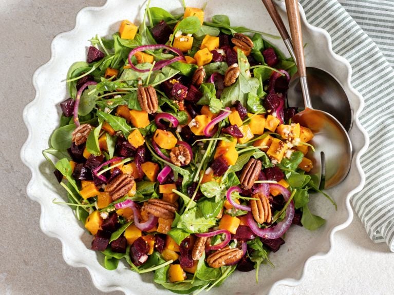 A scalloped ceramic bowl filled with a brightly coloured salad of sweet potato cubes, pickled red onion rings, and arugula.