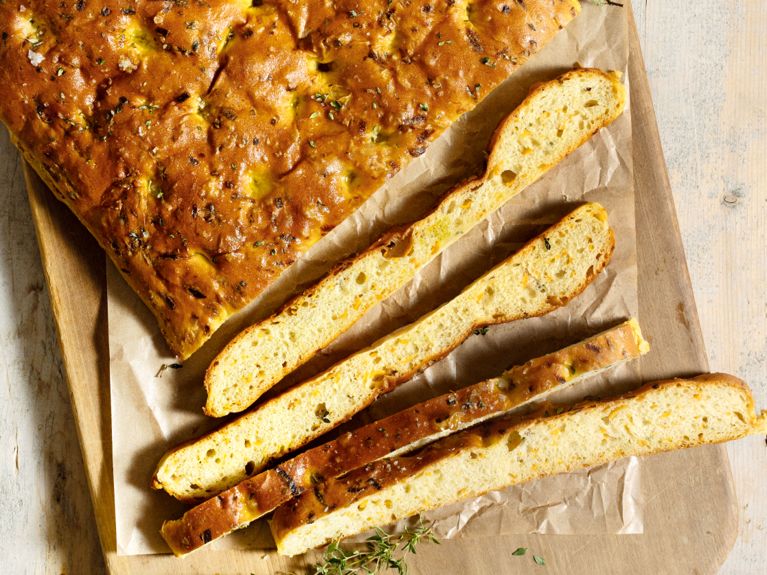A large sheet of light orange focaccia covered in thyme and sliced thin.