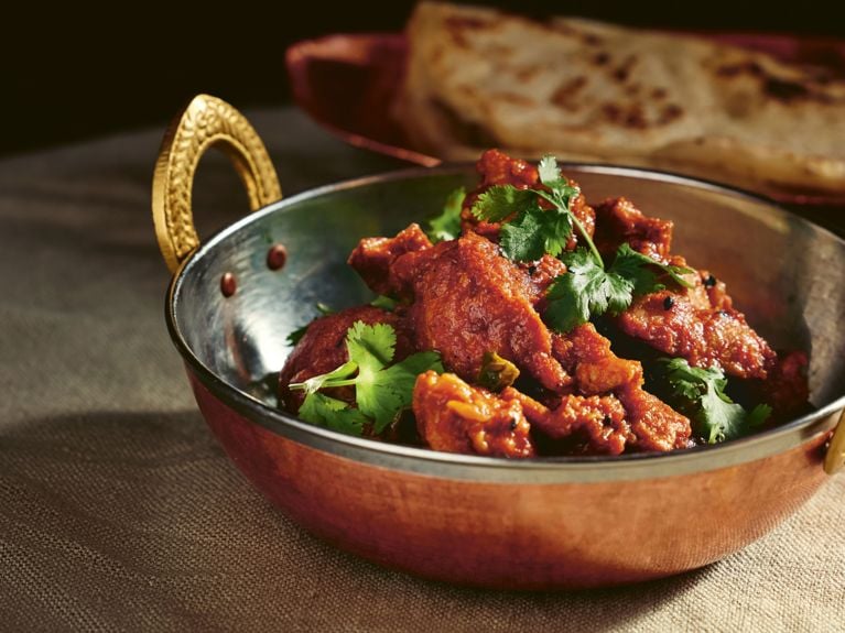 A copper bowl filled with kadhai curried chicken topped with freshly chopped cilantro leaves from Vikram Vij's new cookbook, My New Indian Kitchen.