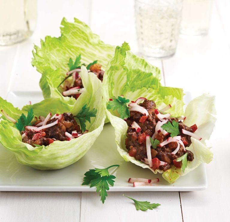 Pomegranate Beef Lettuce Wraps on a white plate; the wraps are made with quick pickled radishes; iceberg lettuce; lean ground beef; dried apricots and more for a post on an easy Pomegranate Beef Lettuce Wraps recipe