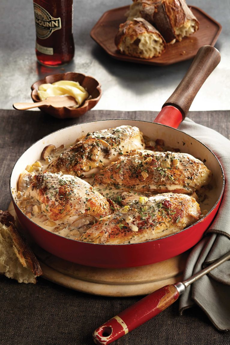 Coq au vin blanc in a red skillet; the chicken is made with skin-on, bone-in chicken breasts; mushrooms; celery stalks; garlic; onion; white wine; thyme; rosemary and cream for a post on an easy one-pan coq au vin blanc recipe