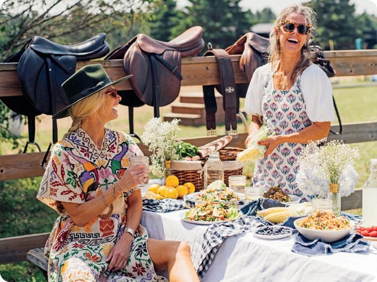 Rebecca and Mandy Wolfe of Mandy's Salads sitting at a picnic table spread with salads on a ranch.