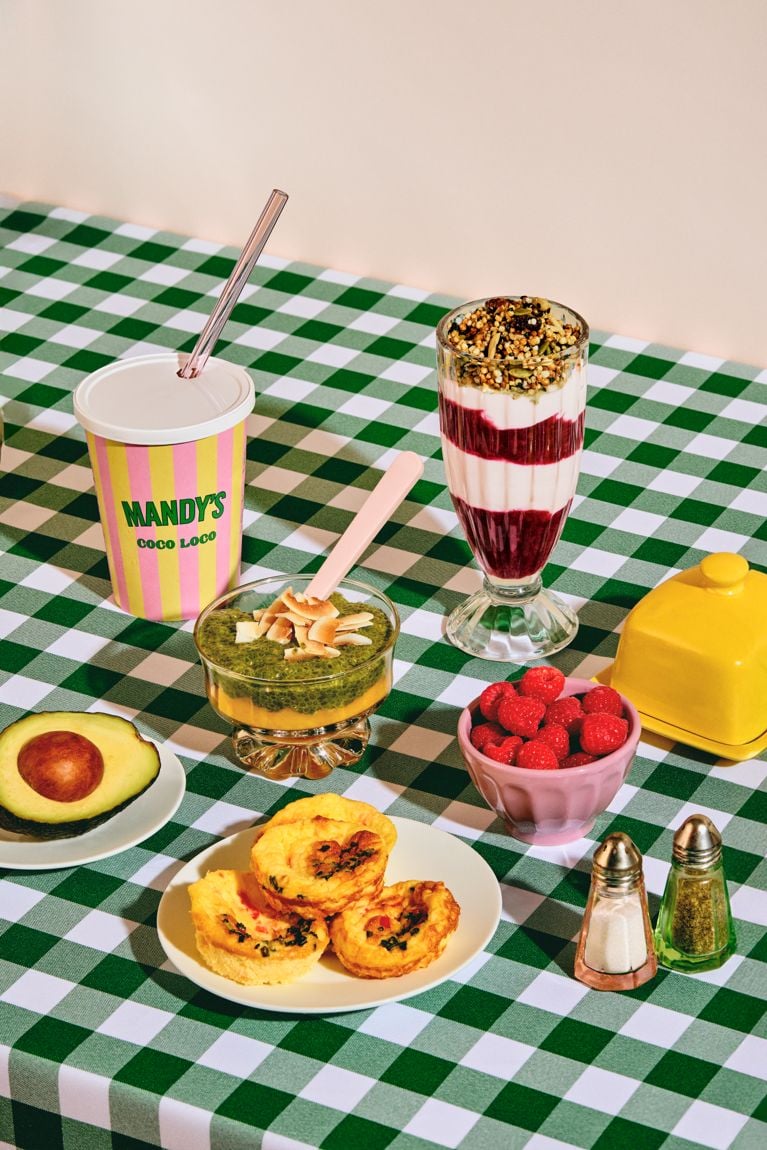 A select of breakfast items sold at Mandy's Salads—including a smoothie, chia pudding, yogurt parfait and egg bites, on a green checkered tablecloth.