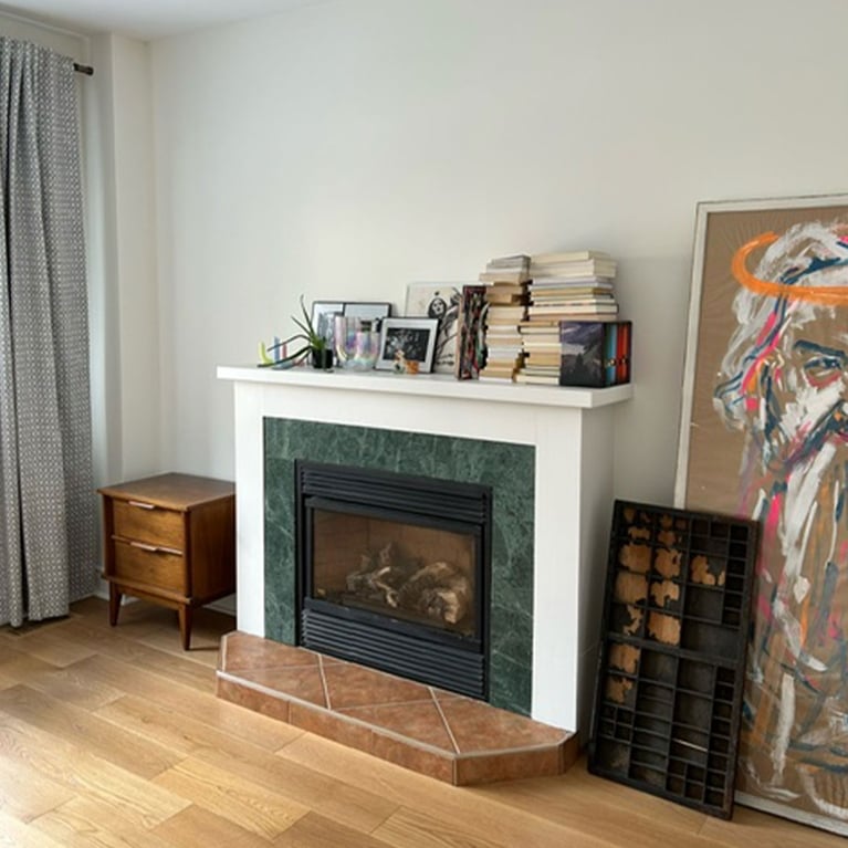 An empty living room painted white with a green tiled fireplace and books.