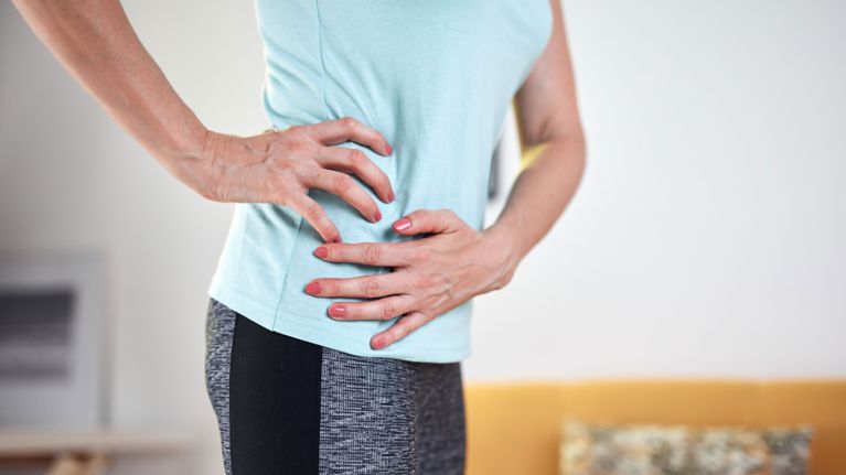 A woman in athletic wear holding her hip, for a story about menopause hip pain