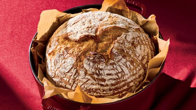 A loaf of 100% whole-white no-knead bread in a red dutch oven lined with parchment paper