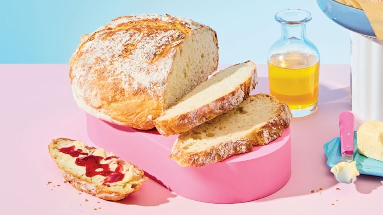 A sliced loaf of no-knead whole-wheat bread sitting on a pink riser
