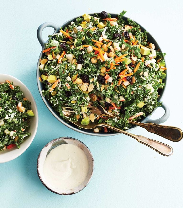 Superfood salad with creamy cashew dressing in a bowl; the salad is made with kale; chickpeas; grated butternut squash; apples; avocados; dried cherries and pepitas with a dressing made of cashews; water; lemon juice and honey for a post on an easy superfood kale salad recipe
