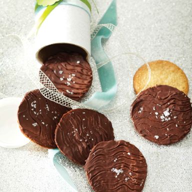 Chocolate-Walnut Thins made with ground oats and nuts covered with thin chocolate spilling from a gift cookie tube adorned with blue and green ribbon for a post on a delicious Chocolate-Walnut Thins recipe
