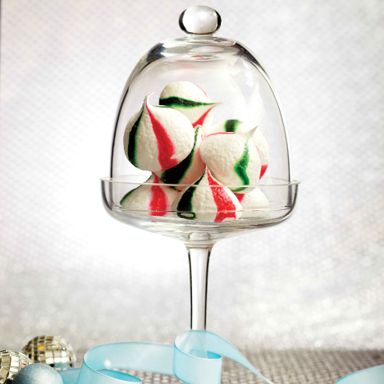 Peppermint Meringue Kisses, made of meringues striped with red and green gel food colouring in a glass serving platter with a glass dome for a post on an easy peppermint meringue kisses recipe